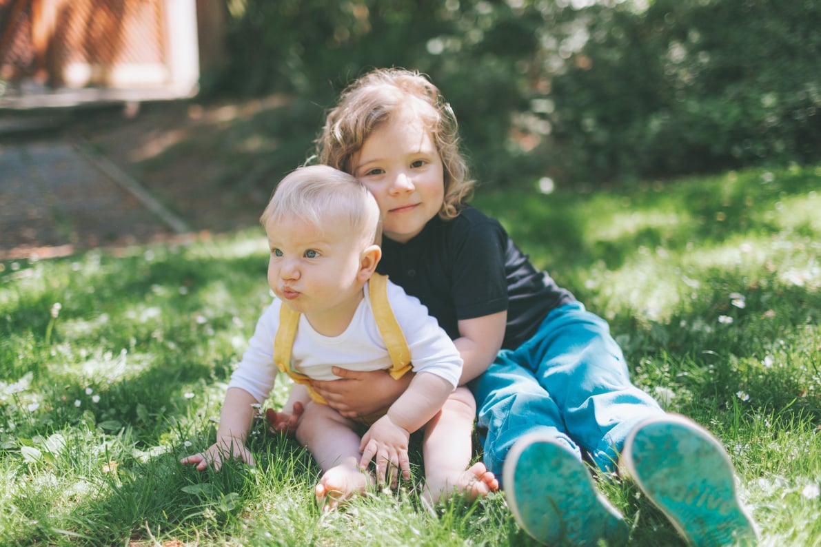 Siblings Hugging While Sitting on Grass